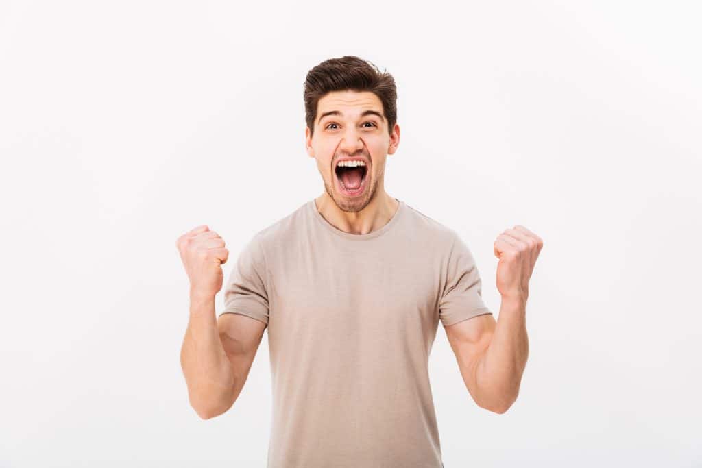 Photo of delighted brunette guy shouting and clenching fists lik