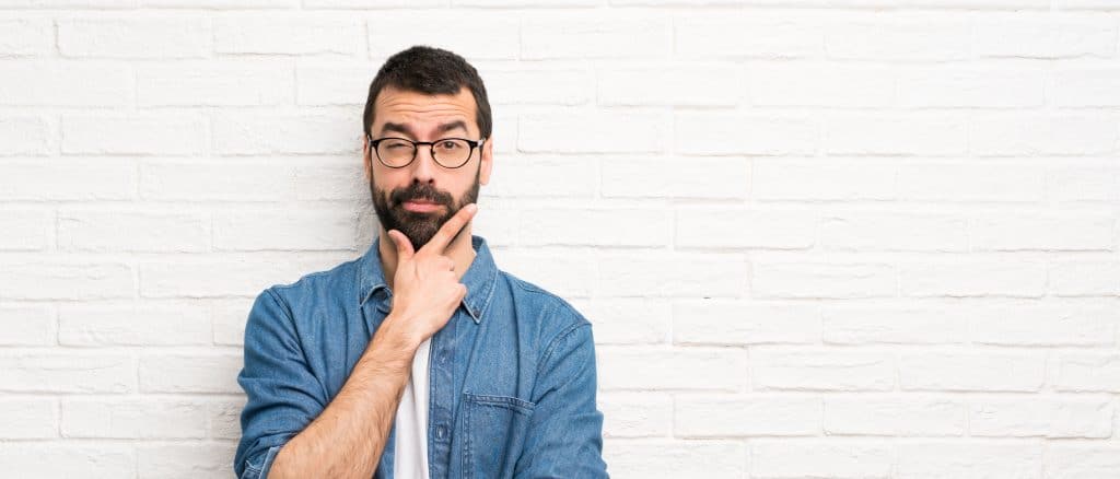 Handsome man with beard over white brick wall thinking