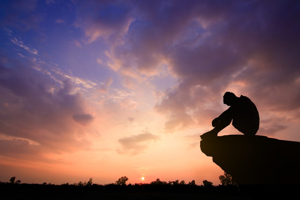 Silhouetted photo Lonely man sitting on cliff He is unhappy an