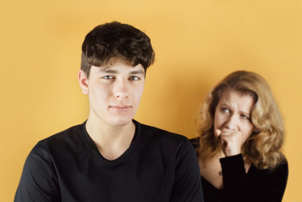 Portrait of a teenage boy, a mother is standing behind him and scolds her son for something, a problem in the relationship between a mother and teenage son