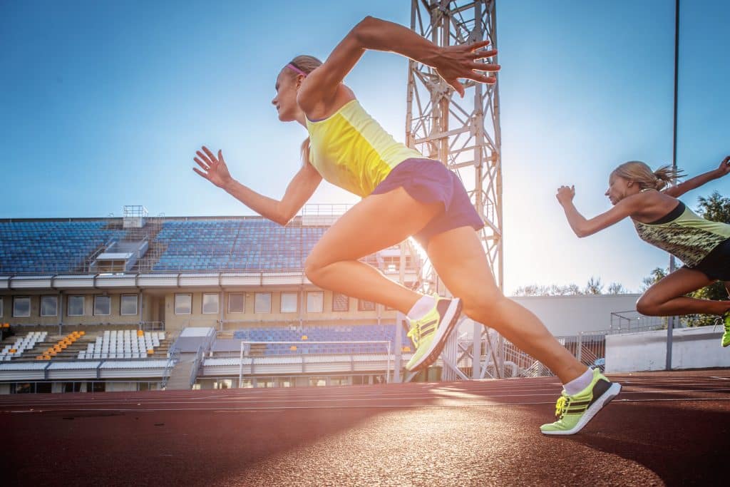 Two female sprinter athletes running on the treadmill race during training in athletics stadium.