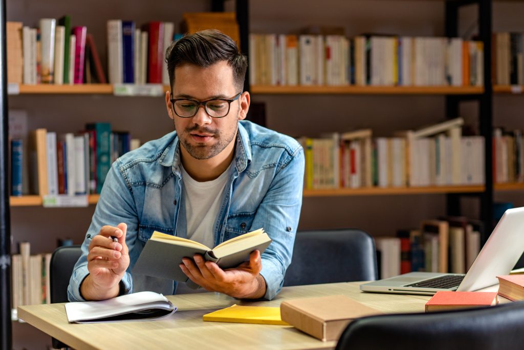 Young male student study in the library reading book.